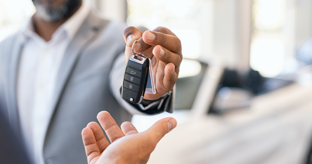 Closeup hand of car dealer giving new car key to customer. Detail of salesman hand giving keys to a client at showroom.
